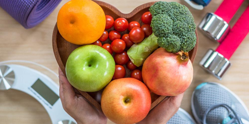 Fruit and vegetables in a heart-shaped bowl and exersise equipment around it